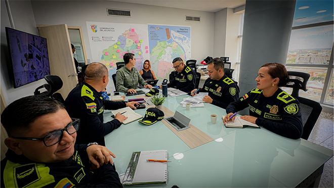 Integrantes de la Policía Nacional y funcionarios de la Gobernación del Atlántico participan en una reunión de trabajo alrededor de una mesa, con mapas y documentos, para coordinar acciones de fortalecimiento institucional y seguridad ciudadana.