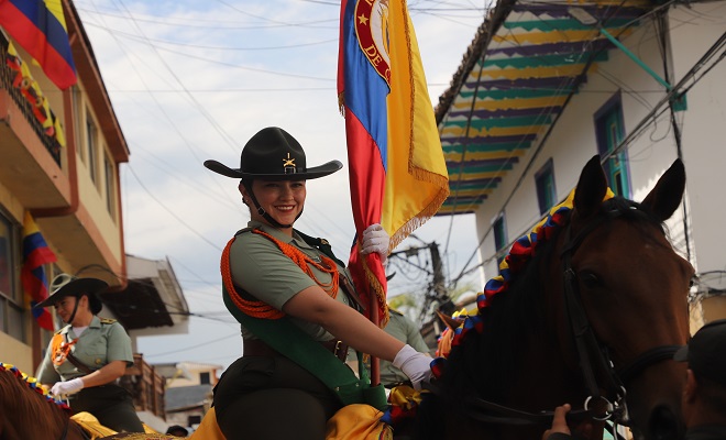 Oficial de la Policía miembro de  Carabineros montada a caballo con la bandera de Colombia 