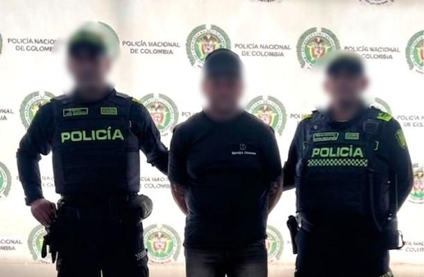 Dos funcionarios policiales con un ciudadano capturado frente al pendón institucional 
