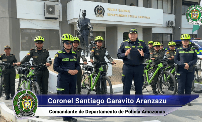Un policía habla mientras está acompañado por dos policías femeninas con casco; detrás de ellos hay más policías de pie que sujetan bicicletas de color verde.