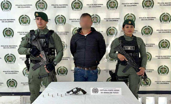 Dos policias con un hombre capturado en el medio, y un arma de fuego en una mesa