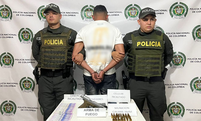 Dos uniformados, un capturado en el medio y encima de una mesa elementos incautados, arma de fuego, dinero, munici&oacute;n y un celular