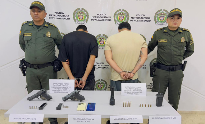 dos policía con dos capturados  y una mesa con dos armas de fuego y  celulares