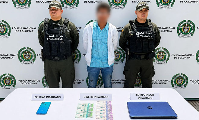 La imagen muestra a dos uniformados del GAULA de la Policía Nacional junto a una persona capturada, cuya identidad está protegida. En la parte inferior se presentan los elementos incautados durante el procedimiento: un teléfono celular, dinero en efectivo y un computador portátil