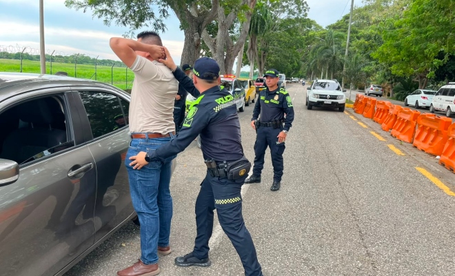 Dos funcionarios policiales realizando registro a persona a un ciudadano junto a un vehículo color gris   