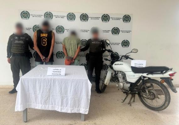 Dos policías junto a dos hombres capturados y una motocicleta al lado