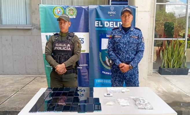 Funcionario del Gaula de la policia acompañado de funcionario del Inpec y una mesa con celulares y cargadores