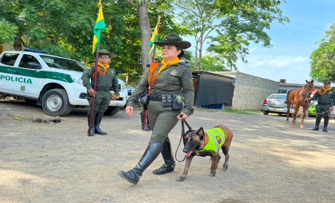 una señora oficial con  un perro en calle de honor al fondo un equino  y un uniformado de la Policía Nacional  
