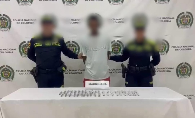 Dos funcionarios policiales con un ciudadano capturado frente a una mesa con elementos estupefacientes incautados 