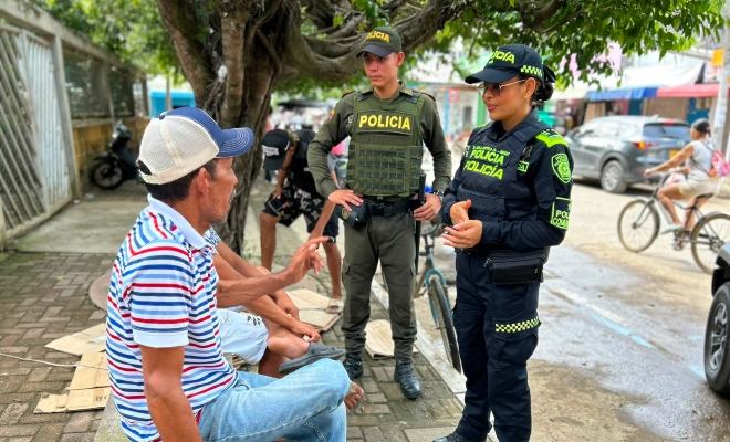 Una funcionaria policial y auxiliar de policía hablando con dos ciudadanos en parque brindando recomendaciones de seguridad