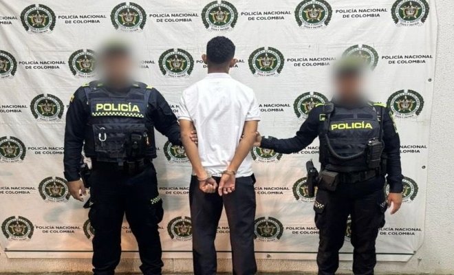 Dos funcionarios policiales con un ciudadano capturado frente a pend&oacute;n institucional 