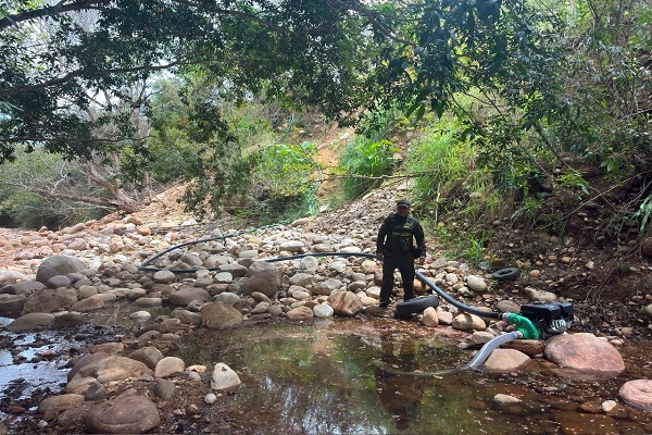 Un policía se encuentra en la ribera de un río junto a una motobomba