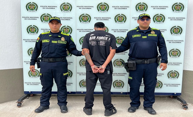 Una persona de espaldas capturada por el delito de concierto para delinquir y homicidio y dos Polic&iacute;as brindando seguridad