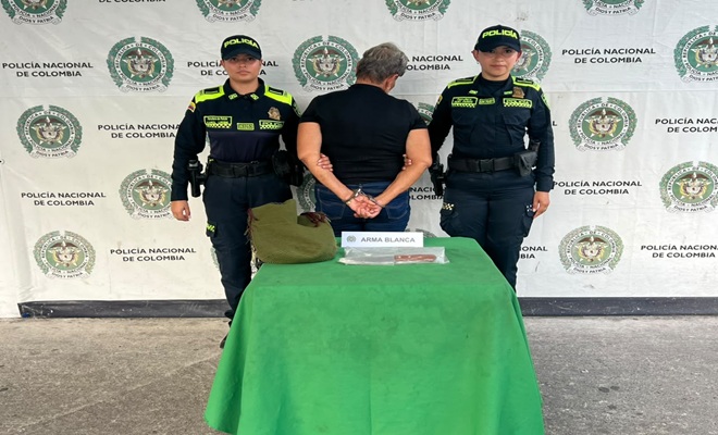 Dos Policías prestando seguridad a una persona capturada por el delito de homicidio en Barrancabermeja y un arma blanca incautada. 