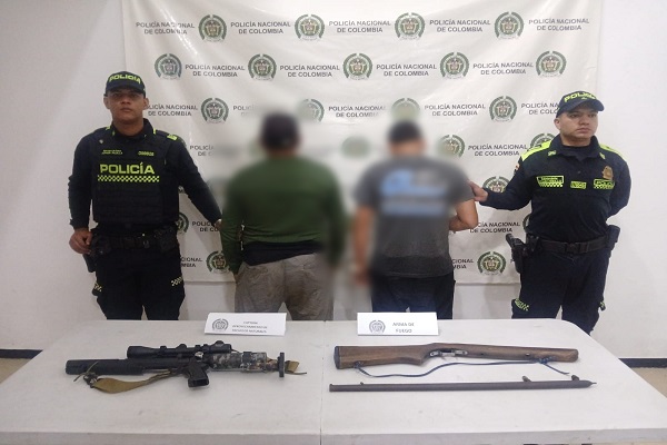 Dos funcionarios presentan a dos capturados junto a un rifle y una escopeta incautados