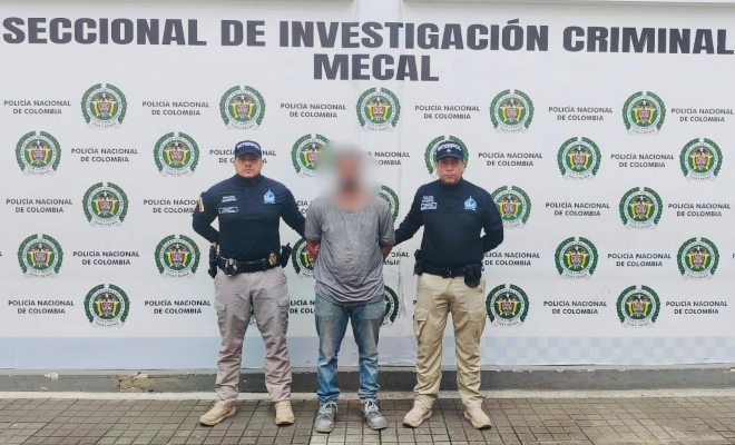 hombre con comiseta gris, pantalon azul claro y dos policias