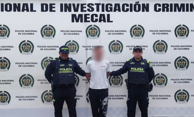 hombre con camiseta blanca y pantalon negro custodiado por dos policias