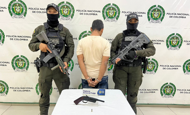 Hombre capturado en medio de dos Policías y un arma de fuego encima de una mesa