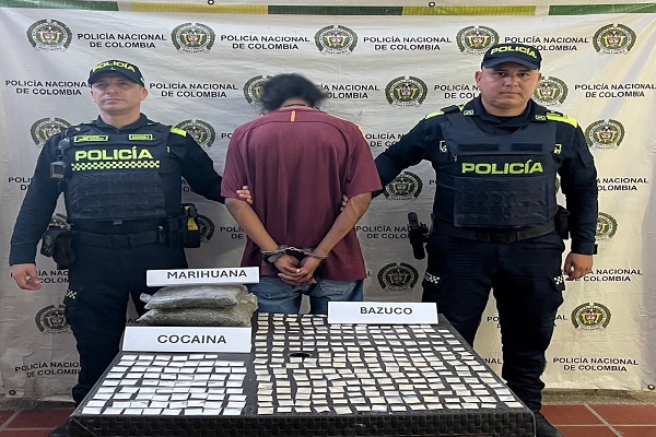 Dos policías custodian a un capturado junto a una mesa con sustancias estupefacientes incautadas