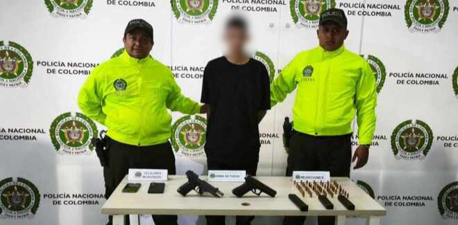 Persona capturada por la Polic&iacute;a Nacional con dos funcionarios, junto a armas y munici&oacute;n incautadas sobre una mesa.
