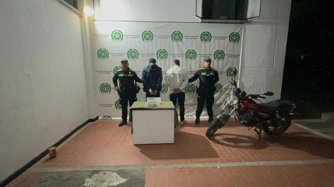 Dos hombres capturados, uno de chaqueta azul y otro de chaqueta blanca en medio de dos policias