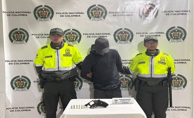 Un ciudadano capturado, esposado y con dos uniformados de la Policía en cada lado, asi como un revolver incautado