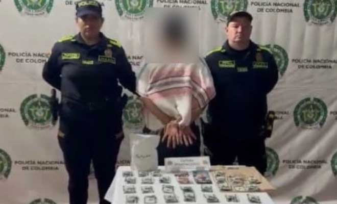 Hombre capturado en medio de dos polic&iacute;as, en frente mesa con estupefacientes incautados