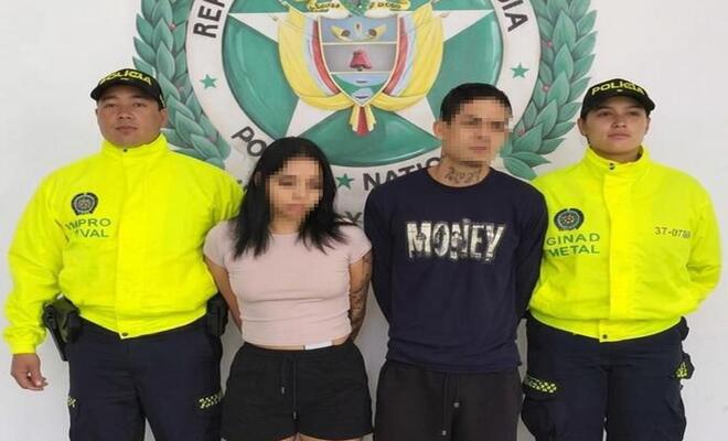Cuatro personas de pie frente a un fondo institucional de la Policía Nacional de Colombia; dos personas en el centro y dos personas uniformadas a los lados.