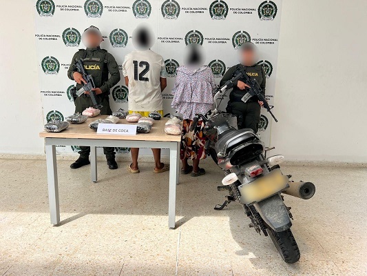 Dos personas capturadas junto a dos polic&iacute;as, una motocicleta y una mesa donde est&aacute;n los elementos incautados 