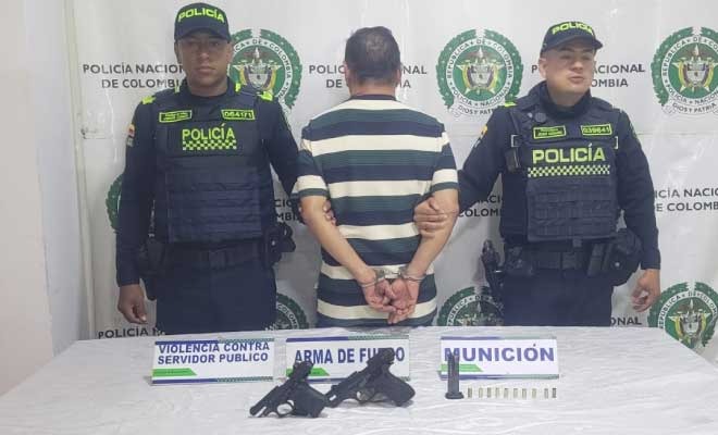 Hombre capturado en medio de dos Policías, en frente armas incautadas