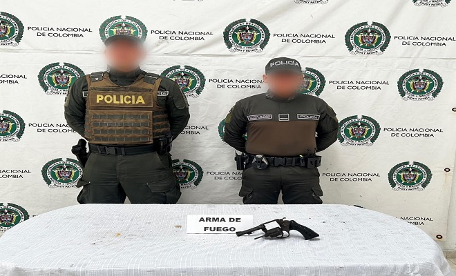 Dos policías presentan arma de fuego tipo revólver incautada sobre una mesa 