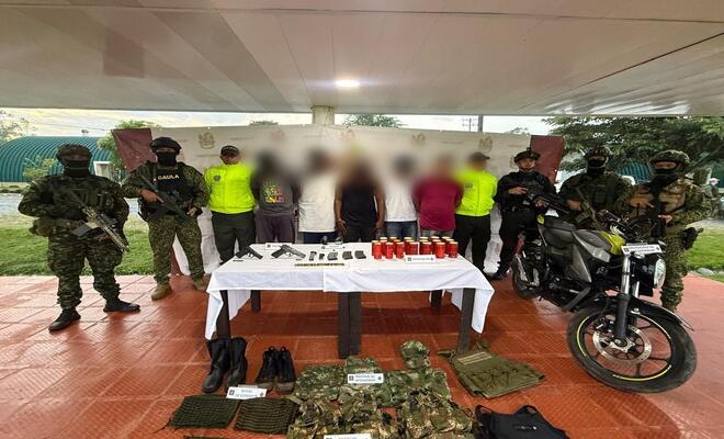 Cinco personas capturadas esposadas con material bélico incautado y uniformados de la Policía Nacional y el Ejercito en cada lado respectivamente  