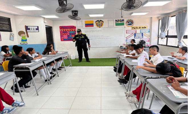 Varios estudiantes están sentados alrededor de una mesa en sus sillas, con un policía de pie frente a ellos