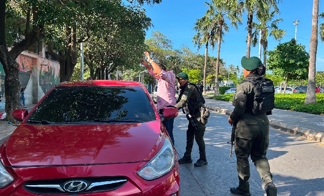 Un vehículo rojo se encuentra detenido en una vía, mientras varios uniformados realizan labores de seguridad y control