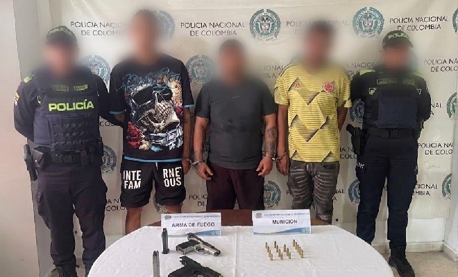 Dos Polic&iacute;a custodian a tres individuos, presentado junto con el material b&eacute;lico incautado.