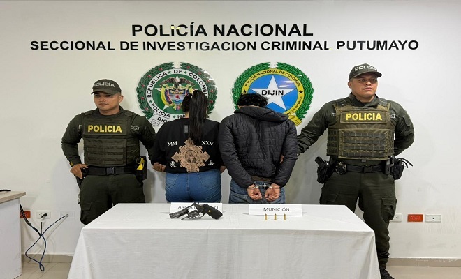 Dos policías y en medio un hombre y una mujer capturados frente a una mesa donde hay un revólver incautado en operativo policial